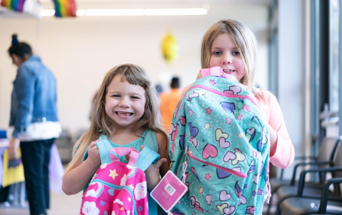 Two young girls hold up backpacks