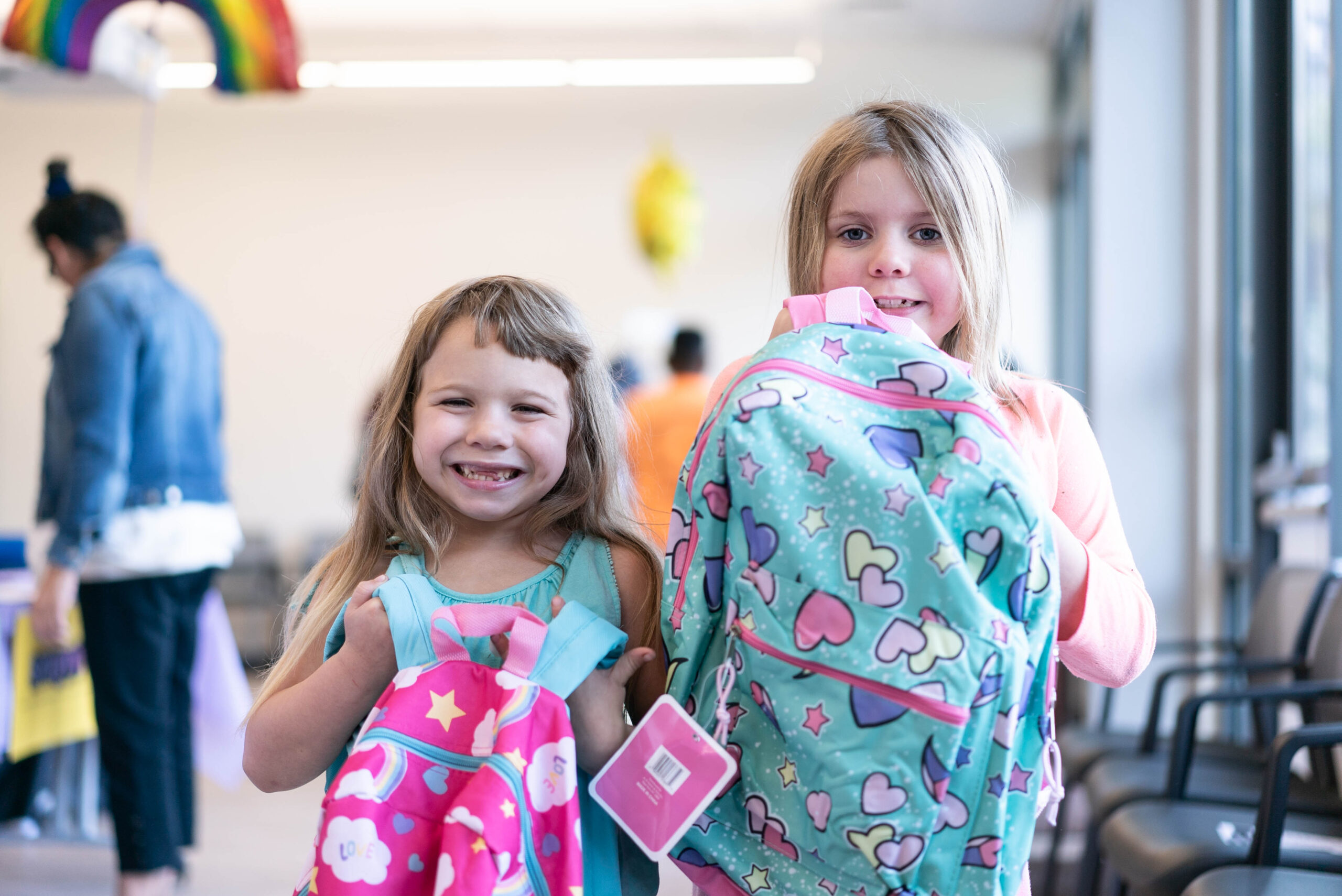Two young girls hold up backpacks